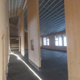 Nord-House - Wnętrze w trakcie budowy domu szkieletowego: widoczne drewniane ściany działowe z otworami okiennymi, metalowa konstrukcja dachu, oraz surowa podłoga z folią budowlaną.