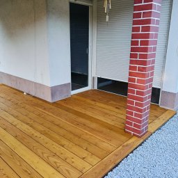 Nord-House - Nowa, drewniana powierzchnia przylegająca do budynku z ceglanym filarem, otoczona drobnym żwirem.