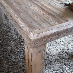 Nord-House - Stół z surowego, bielonego drewna z grubymi nogami, wykonany w Siedlęcinie, na tle beżowej kanapy i szarego dywanu z długim włosiem.