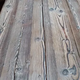 Blat stołu z desek z wyraźnym usłojeniem, wykończony w odcieniach szarości i brązu, z widocznymi sękami i szczelinami.