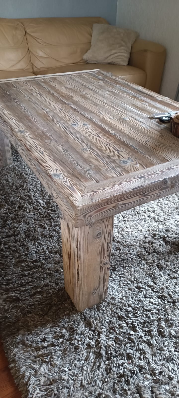 Stół z surowego, bielonego drewna z grubymi nogami, wykonany w Siedlęcinie, na tle beżowej kanapy i szarego dywanu z długim włosiem.