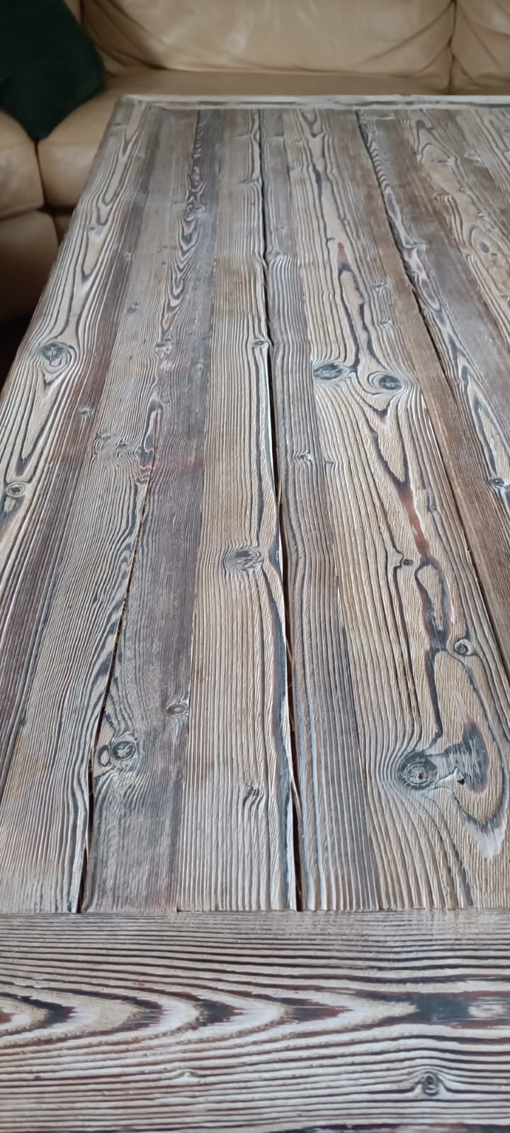 Blat stołu z desek z wyraźnym usłojeniem, wykończony w odcieniach szarości i brązu, z widocznymi sękami i szczelinami.