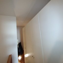 Krzysztof Bieniek - Świeżo pomalowana na biało ściana w mieszkaniu, widoczny fragment szafy wnękowej i czarny worek na śmieci w tle.