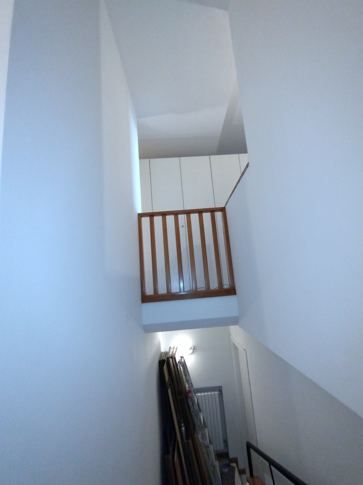 Wnętrze domu po malowaniu: białe ściany, drewniana balustrada na antresoli, schody w dół, widoczne ramy obrazów opartych o ścianę.