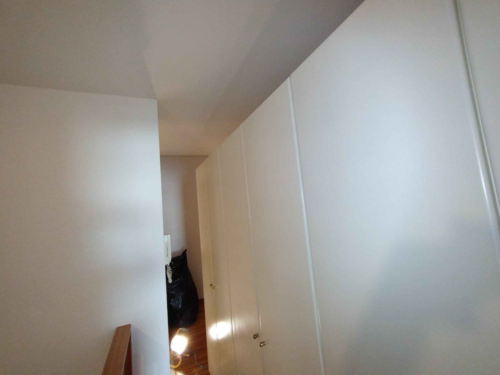Świeżo pomalowana na biało ściana w mieszkaniu, widoczny fragment szafy wnękowej i czarny worek na śmieci w tle.