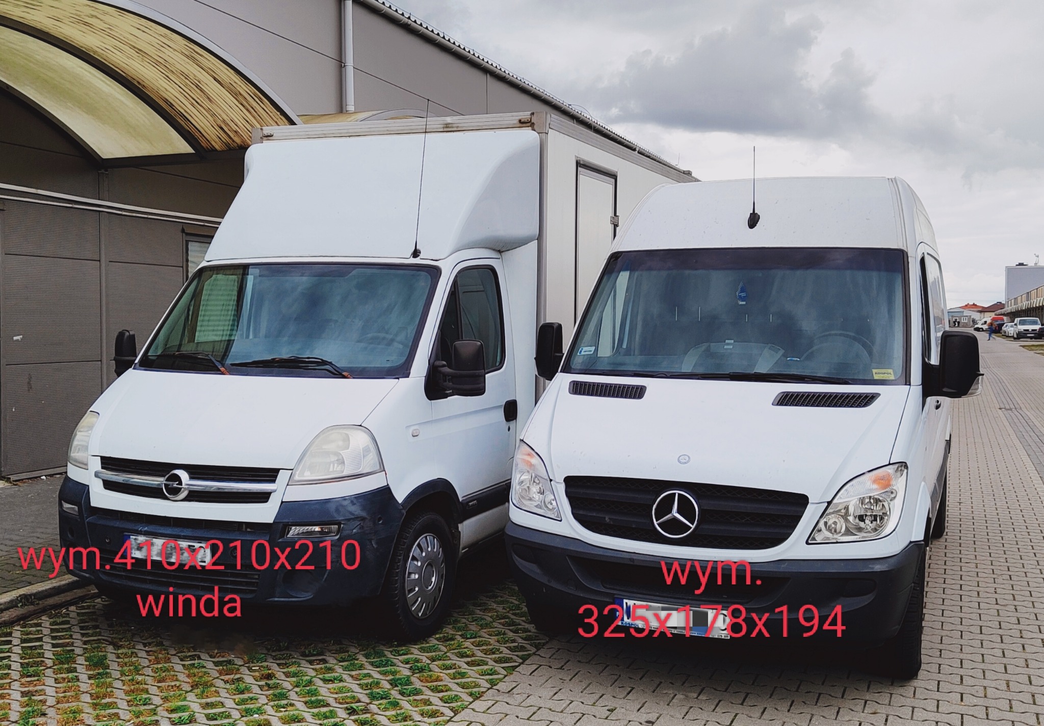 Dwa białe samochody dostawcze, Opel i Mercedes, zaparkowane obok siebie na brukowanym placu. Opel ma windę załadunkową i widoczne ślady użytkowania na zderzaku.