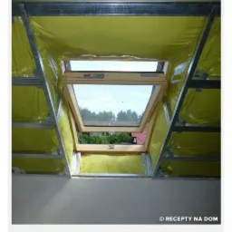 Wnętrze poddasza z oknem dachowym w trakcie prac wykończeniowych, widoczna metalowa konstrukcja rusztu i żółta folia izolacyjna, przez okno widać fragment zieleni.