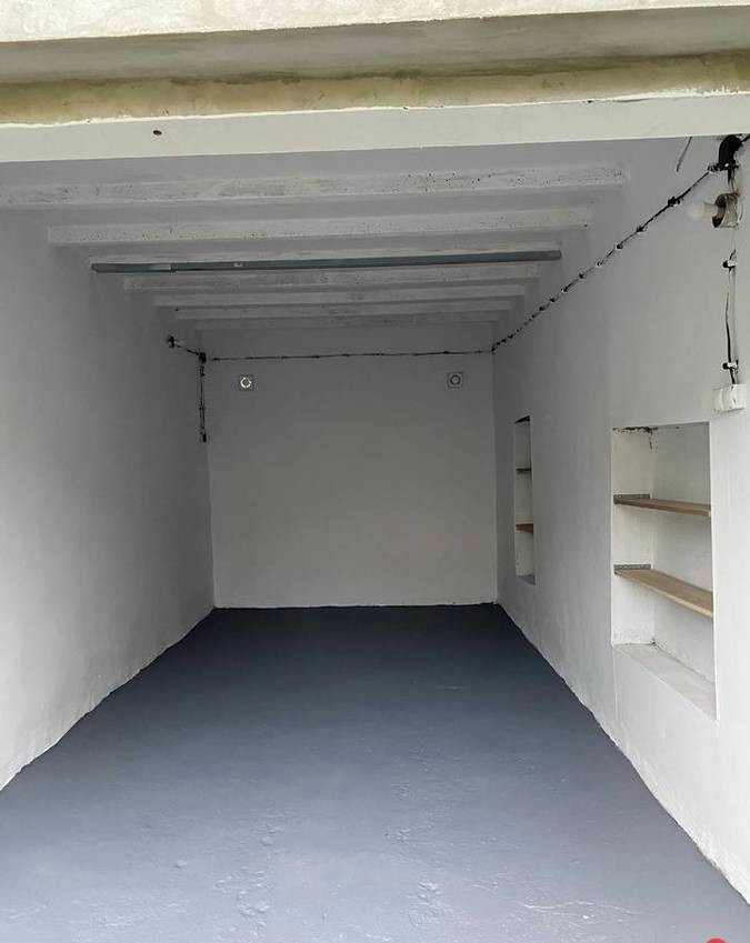 Wnętrze garażu po malowaniu podłogi na szaro, widoczne białe ściany i sufit z belkami oraz wnęka z drewnianymi półkami.