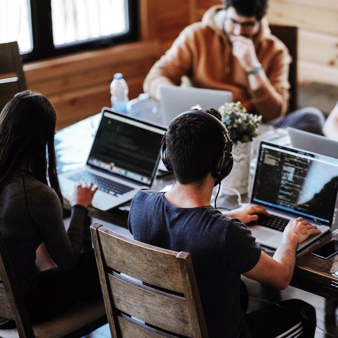 Trzech programistów pracuje przy laptopach w jasnym, przestronnym biurze. Jeden z nich ma na uszach słuchawki.