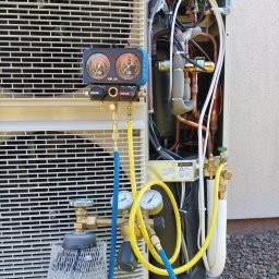 Instacjekompleksowo.pl- Tze.pl Wrocław - Otwarta obudowa klimatyzatora z widocznymi miedzianymi rurami, przewodami i podłączonym manometrem oraz butlą z gazem chłodniczym podczas serwisu.