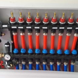 Instacjekompleksowo.pl- Tze.pl Wrocław - Rozdzielacz ogrzewania podłogowego w białej szafce, z przewodami w kolorach czerwonym i niebieskim, z etykietami opisującymi poszczególne obwody grzewcze.