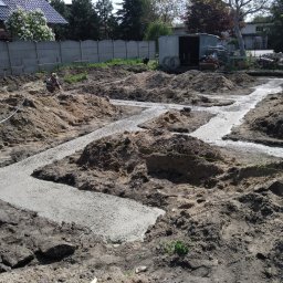 Instacjekompleksowo.pl- Tze.pl Wrocław - Wylane fundamenty pod budynek, widoczny pracownik w oddali, ziemia i piasek w wykopach, szalunki oraz betonowe ścieżki fundamentowe w trakcie realizacji.