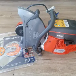 Piła spalinowa do betonu Husqvarna K770 z tarczą diamentową TACTI-CUT S50+ w opakowaniu na drewnianym podłożu.