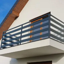 Nowoczesna, pozioma balustrada balkonowa w kolorze grafitowym w Manowie, z widocznymi drewnianymi elementami wykończenia dachu i okien.