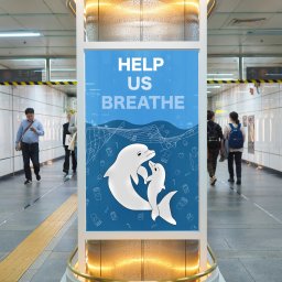 Julia Bobrukiewicz - Plakat w metrze z grafiką dwóch białych delfinów na niebieskim tle, z hasłem 'HELP US BREATHE', otoczonych rysunkami puszek i słomek, promujący kampanię ekologiczną.