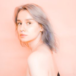 Julia Bobrukiewicz - Portret kobiety z szarymi włosami i kryształkami na twarzy, patrzącej przez ramię na jasnoróżowym tle.