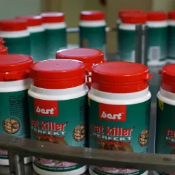 Butelki z preparatem na szczury 'Best Rat Killer Perfekt Granulat' na linii produkcyjnej, widoczne czerwone zakrętki i zielone etykiety.