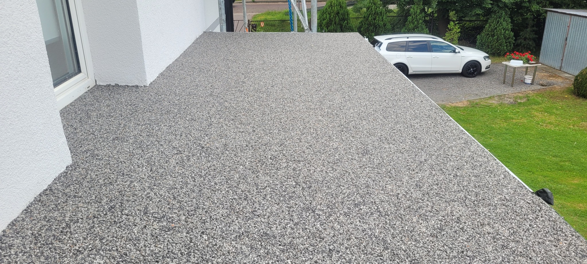 Wykończony taras z szarej żywicy kamiennej, widok z góry, na tle biały samochód osobowy i zielony trawnik.