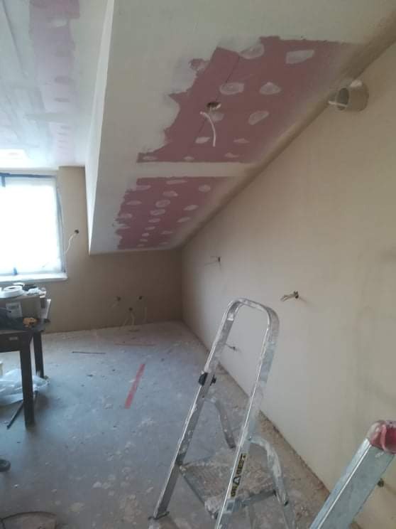 Poddasze w trakcie remontu: widoczne fragmenty sufitu z nałożoną masą szpachlową na łączeniach płyt, drabina aluminiowa, okno w tle, ślady pyłu na podłodze.