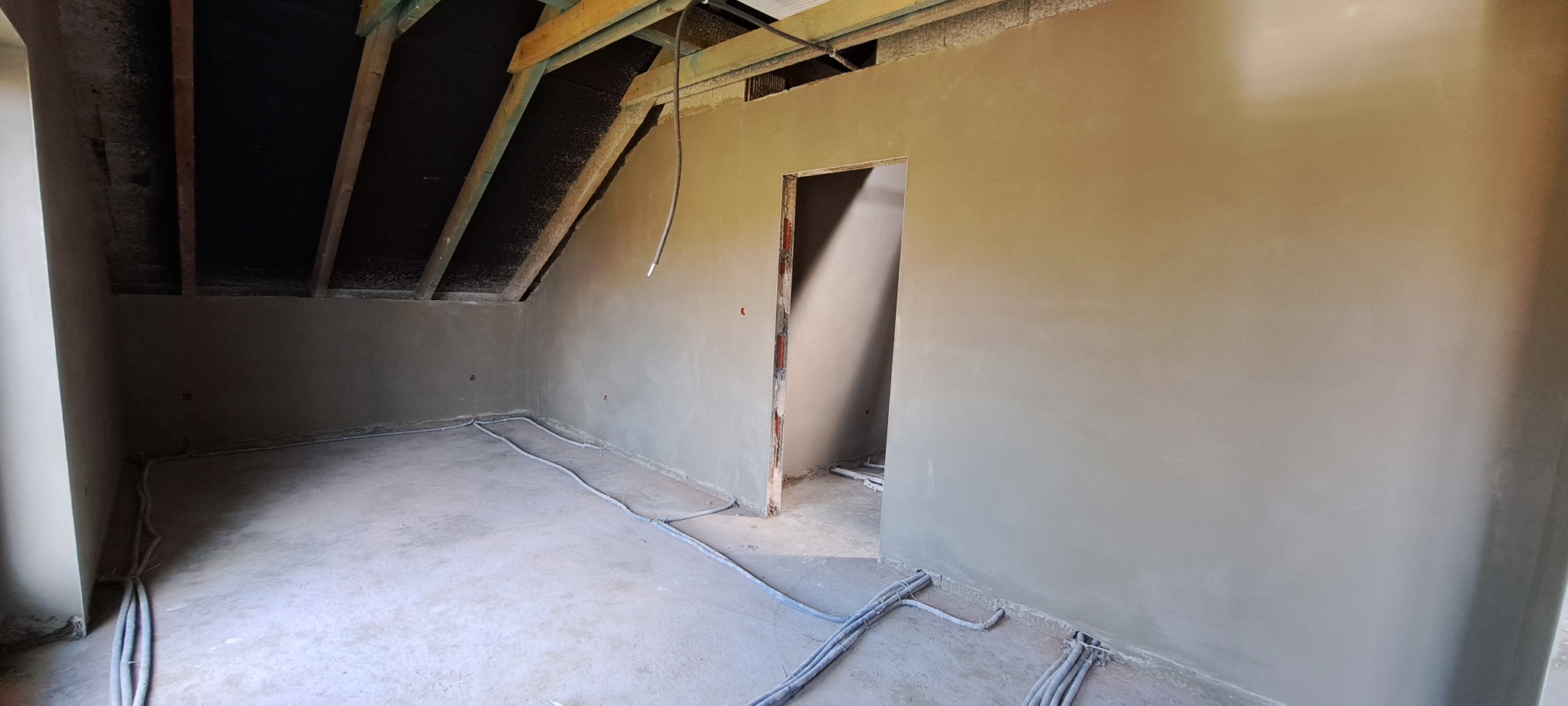 Pokój na poddaszu po nałożeniu gładzi, widoczne kable elektryczne przy podłodze i drewniana konstrukcja dachu.