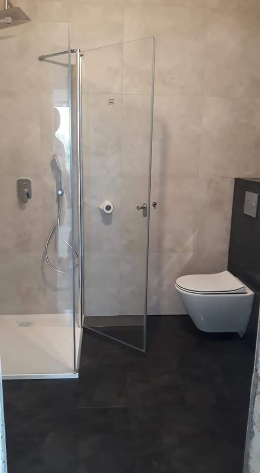 Wykończona łazienka w Warszawie z kabiną prysznicową ze szklanymi drzwiami, podwieszaną toaletą i szarymi płytkami na ścianach.