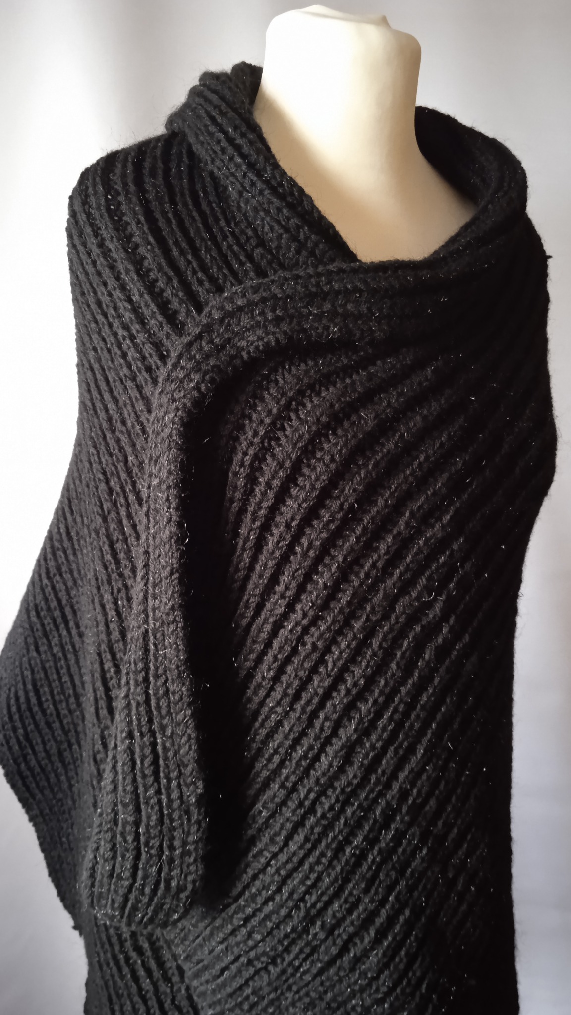 Czarne, grubo dziergane ponczo z wyraźnym wzorem ściegu, prezentowane na manekinie na neutralnym tle.