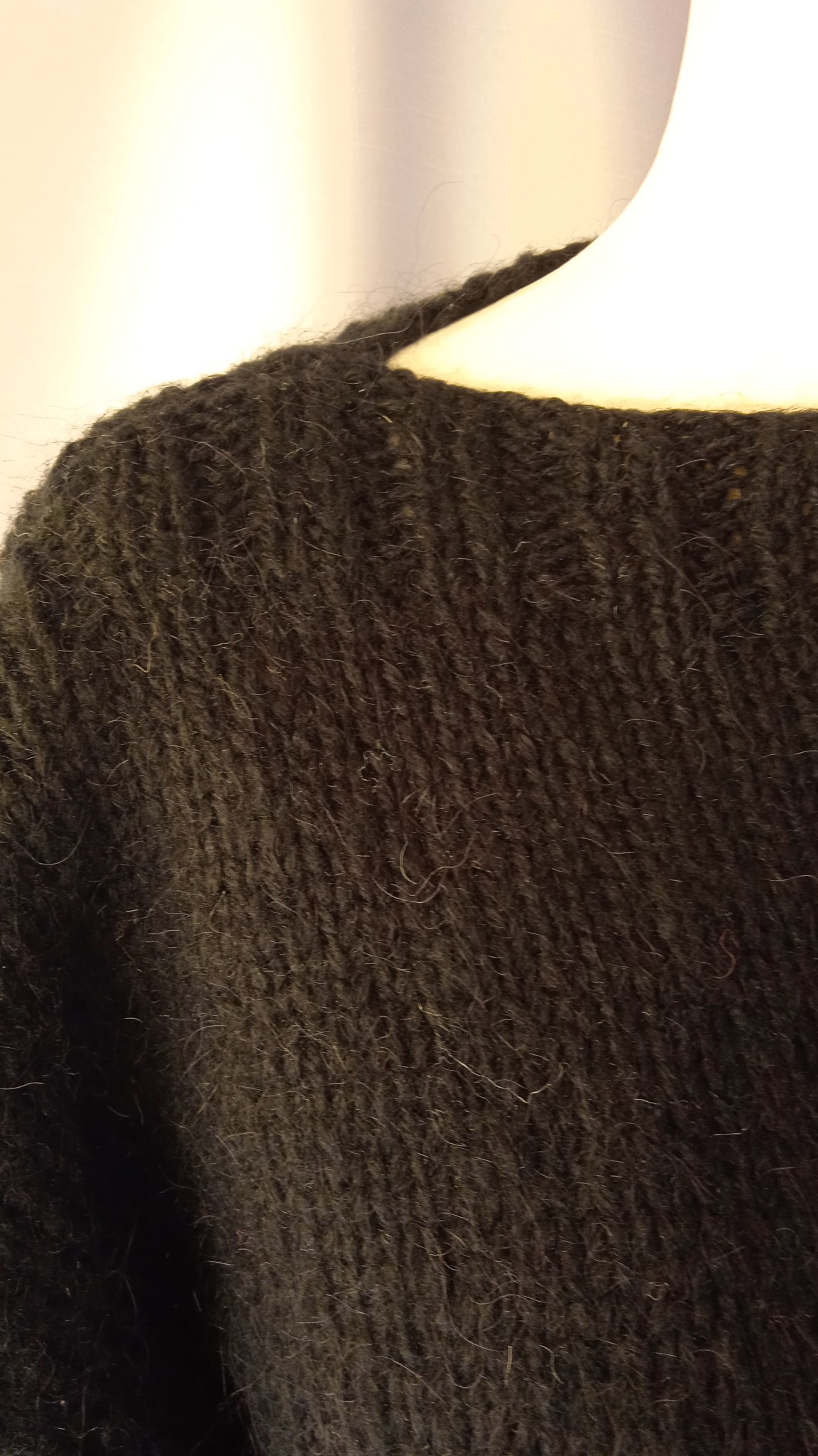 Część czarnego, grubego swetra z widocznym splotem, na manekinie.