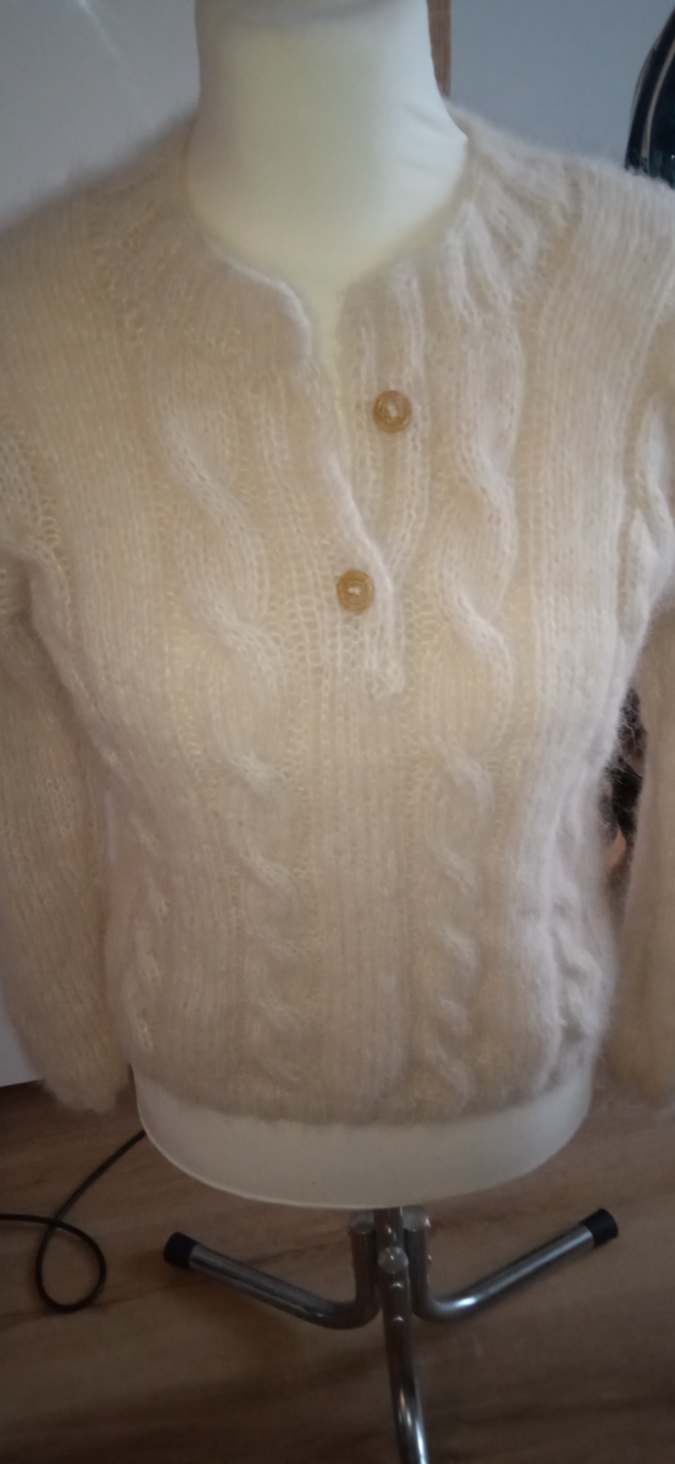 Kremowy, ręcznie robiony sweter z warkoczowym splotem i dwoma jasnobrązowymi guzikami, prezentowany na manekinie.