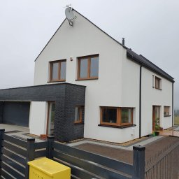 Building Services Sp. z o.o. - Nowoczesny dom jednorodzinny z białą elewacją i czarną cegłą, drewniane okna, szara metalowa brama, widok z zewnątrz w pochmurny dzień.