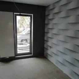 Pokój po odświeżeniu: ściana z trójwymiarową tapetą w odcieniach szarości, pomalowana na ciemnozielono ściana z oknem, przez które widać samochód.