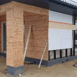 Montaż drewnianej elewacji na budynku w Warszawie, widoczne panele izolacyjne i poziomica oparta o ścianę.