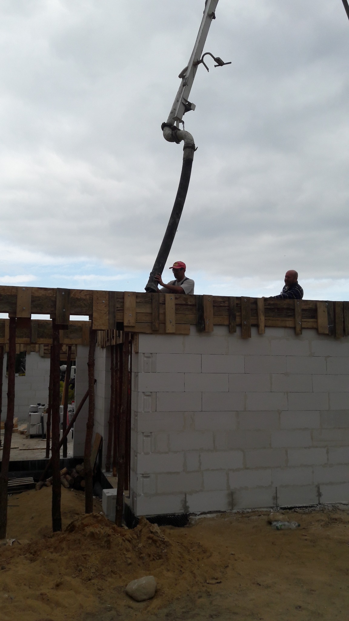Betonowanie ścian domu z betonu komórkowego z użyciem pompy do betonu, widoczni dwaj pracownicy na szalunku.