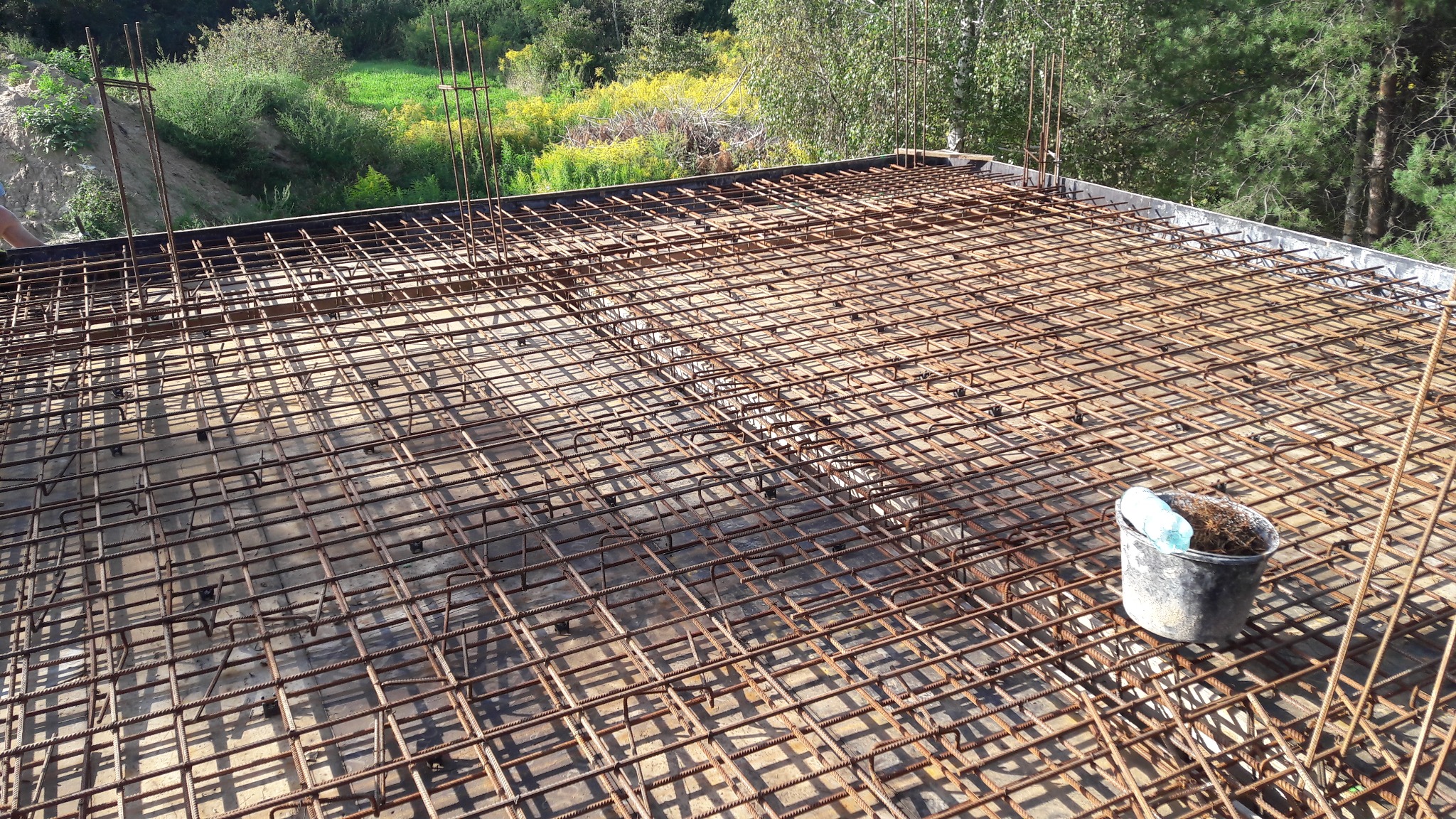 Zbrojenie płyty fundamentowej z widocznym wiaderkiem i zieleniejącym tłem.