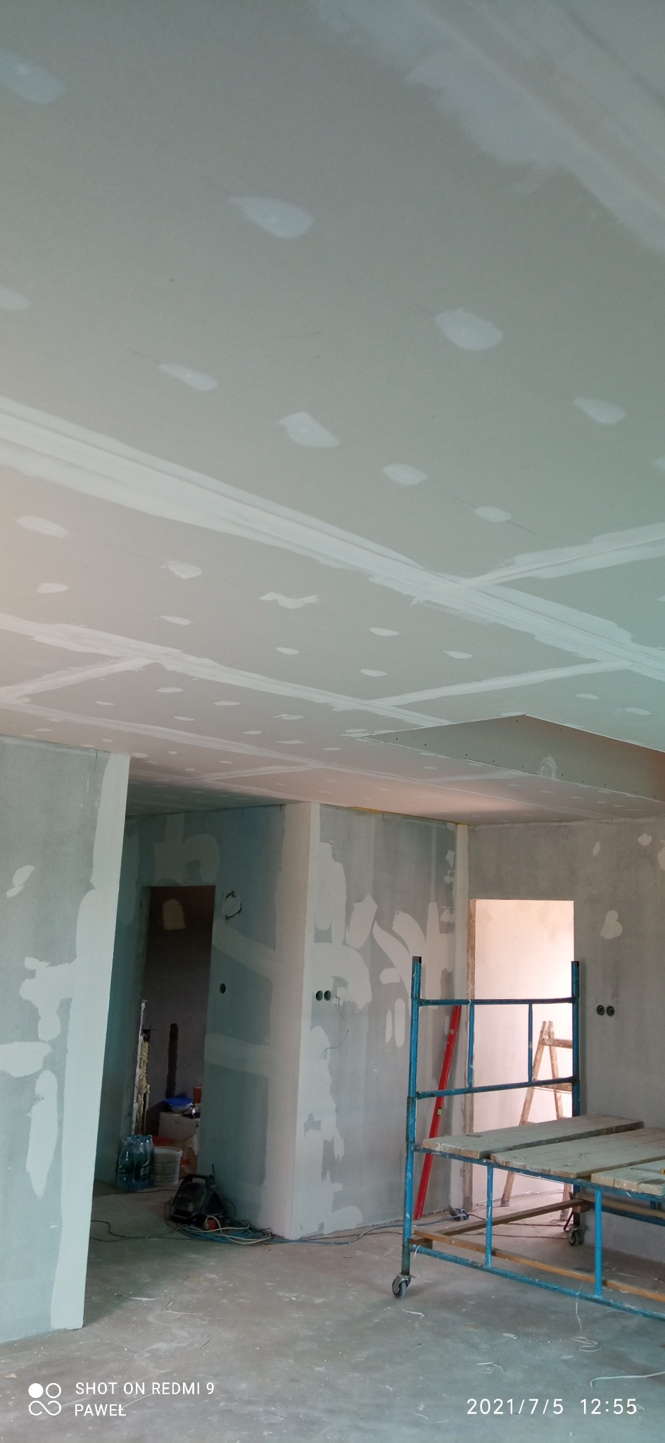 Wnętrze w trakcie prac wykończeniowych: ściany i sufit pokryte płytami gipsowo-kartonowymi, widoczne łączenia szpachlowane, rusztowanie w pomieszczeniu, przygotowane podłoże pod dalsze prace.