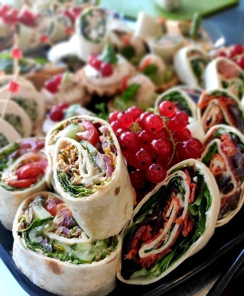 Tortilla wraps z różnymi nadzieniami i świeżymi czerwonymi porzeczkami na czarnym talerzu, widoczne warstwy sałaty, pomidorów, ogórków i innych warzyw.