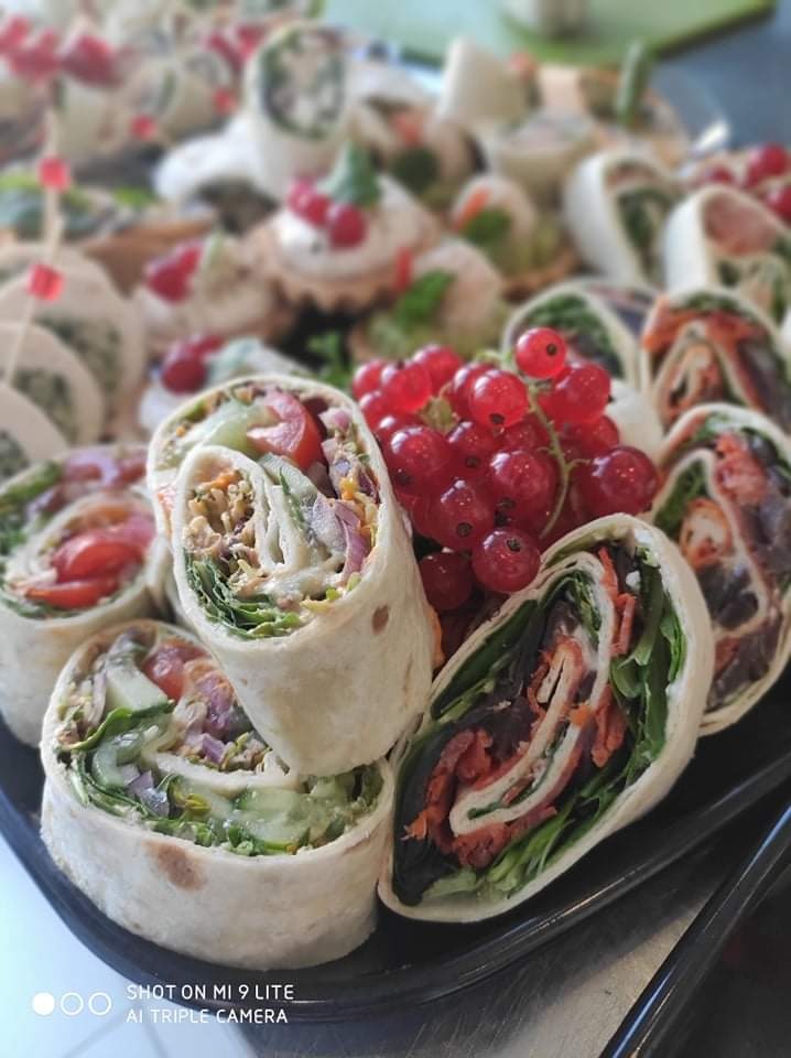 Tortilla wraps z różnymi nadzieniami, dekorowane kiścią czerwonej porzeczki, ułożone na czarnym talerzu.