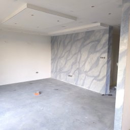 Mar Bud - Wnętrze w trakcie wykańczania: ściana z dekoracyjnym wzorem imitującym marmur, surowa podłoga, widoczne puszki elektryczne i narzędzia. Oświetlenie sufitowe w zabudowie.