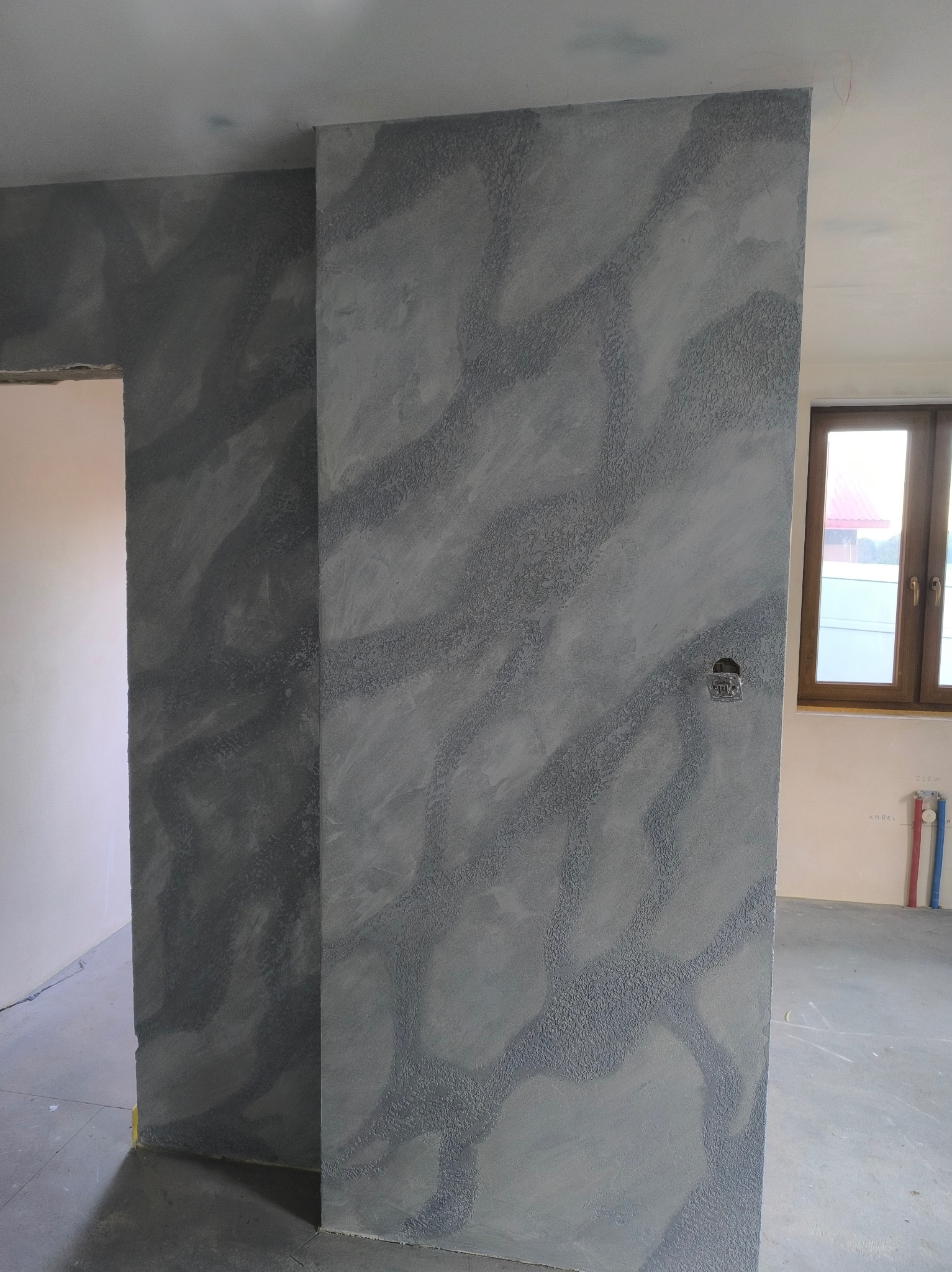 Szara ściana z dekoracyjną fakturą w nowym wnętrzu. Widoczny fragment okna i instalacji. Świeżo wykończone ściany z unikalnym wzorem.