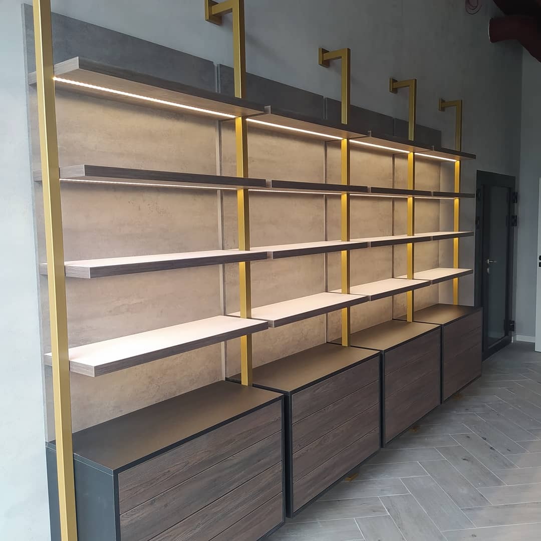 Zabudowa ścienna z szufladami i podświetlanymi półkami w kolorach szarości, brązu i złota, wykonana w Zadworzu.