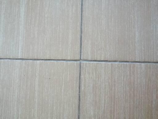 Cztery beżowe płytki podłogowe z szarymi fugami, widoczne z bliska, z delikatną teksturą imitującą drewno.