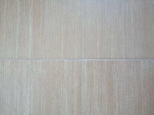 Beżowe, matowe płytki podłogowe z delikatną, pionową strukturą i szarymi fugami, ułożone w kwadrat.