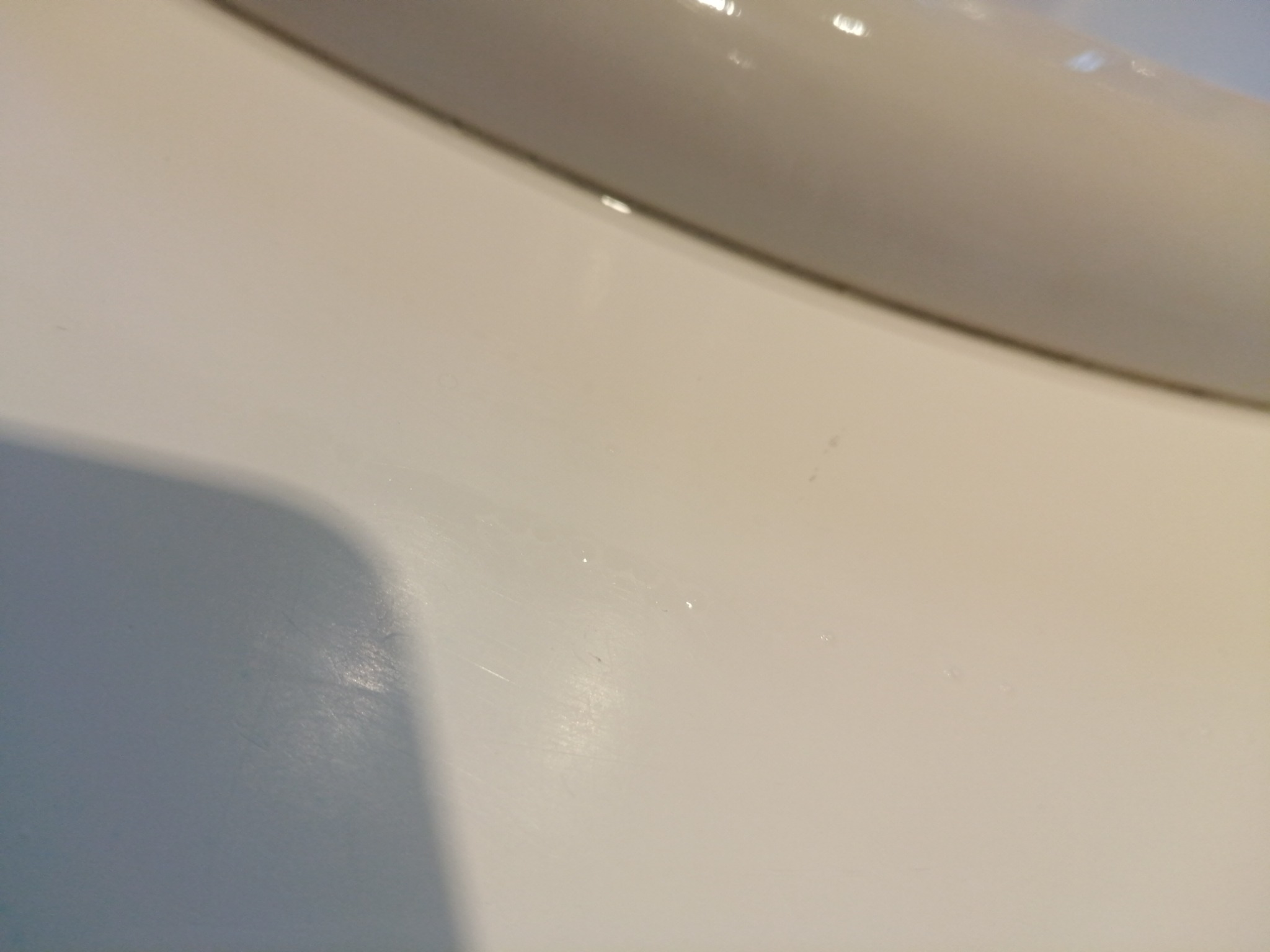 Biała powierzchnia umywalki z widocznymi drobnymi zabrudzeniami i zaciekami, oświetlona górnym światłem.