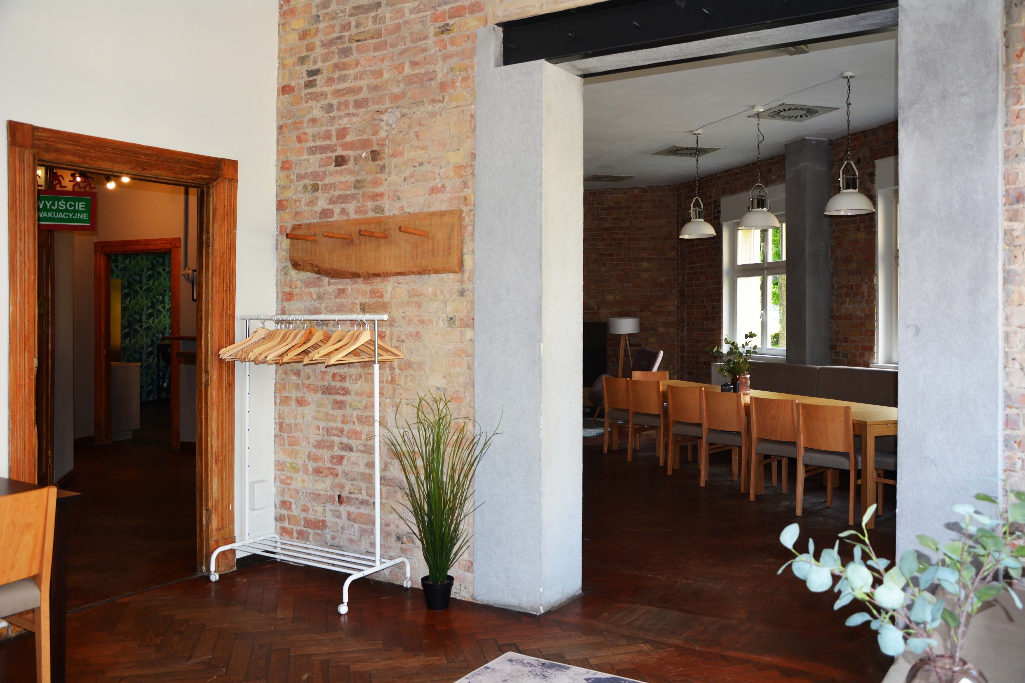 Wnętrze restauracji w Poznaniu z widocznymi drewnianymi stołami, krzesłami i elementami dekoracyjnymi, takimi jak wieszak na ubrania przy wejściu i rośliny doniczkowe, tworzące przytulną atmosferę.