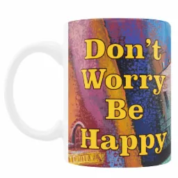 Biały kubek z abstrakcyjnym, kolorowym nadrukiem przedstawiającym budynki i hasłem 'Don't Worry Be Happy' w żółtej czcionce.