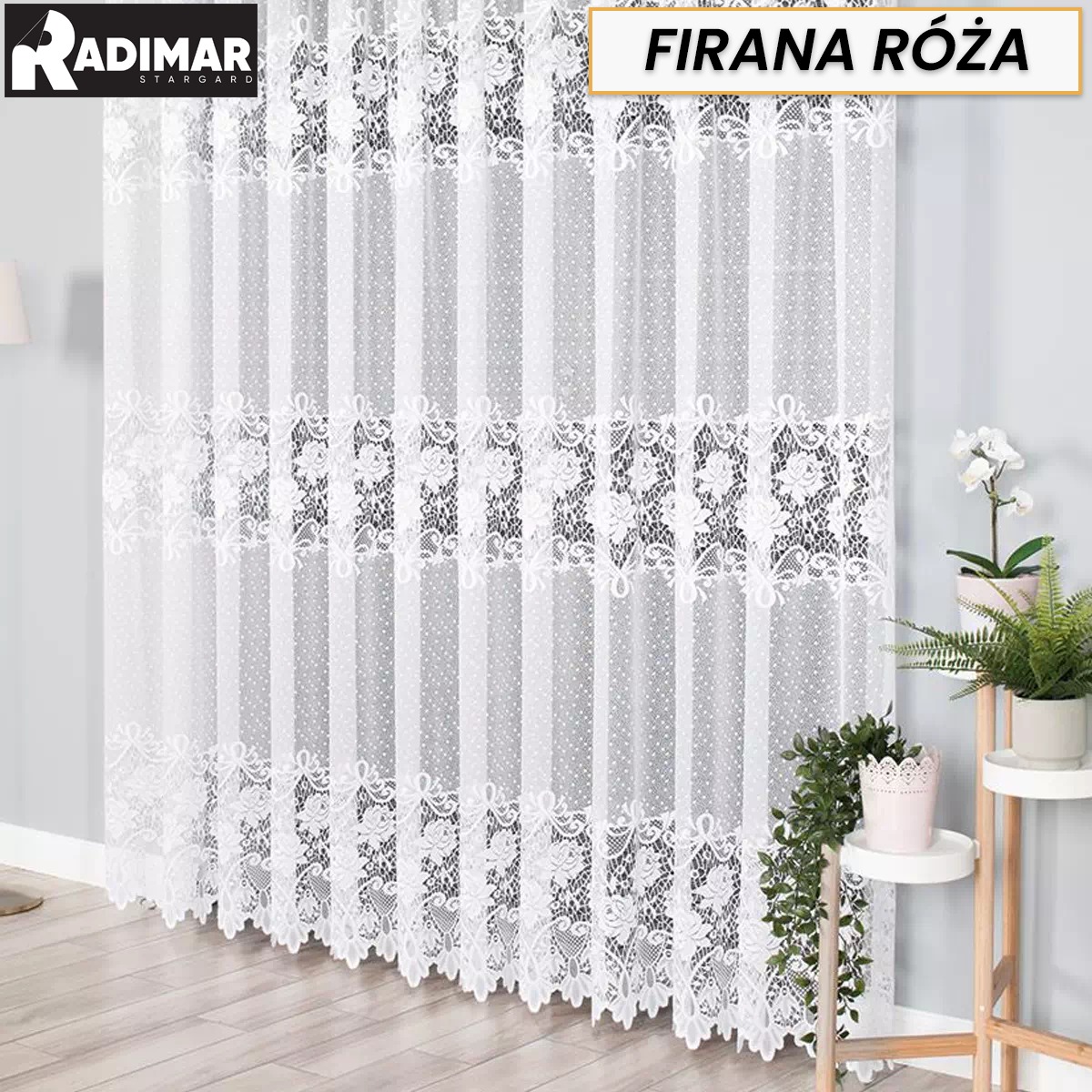 Delikatna, biała, długa firana z koronkowym wzorem i motywem róży, zawieszona w jasnym wnętrzu obok roślin doniczkowych na drewnianym kwietniku.