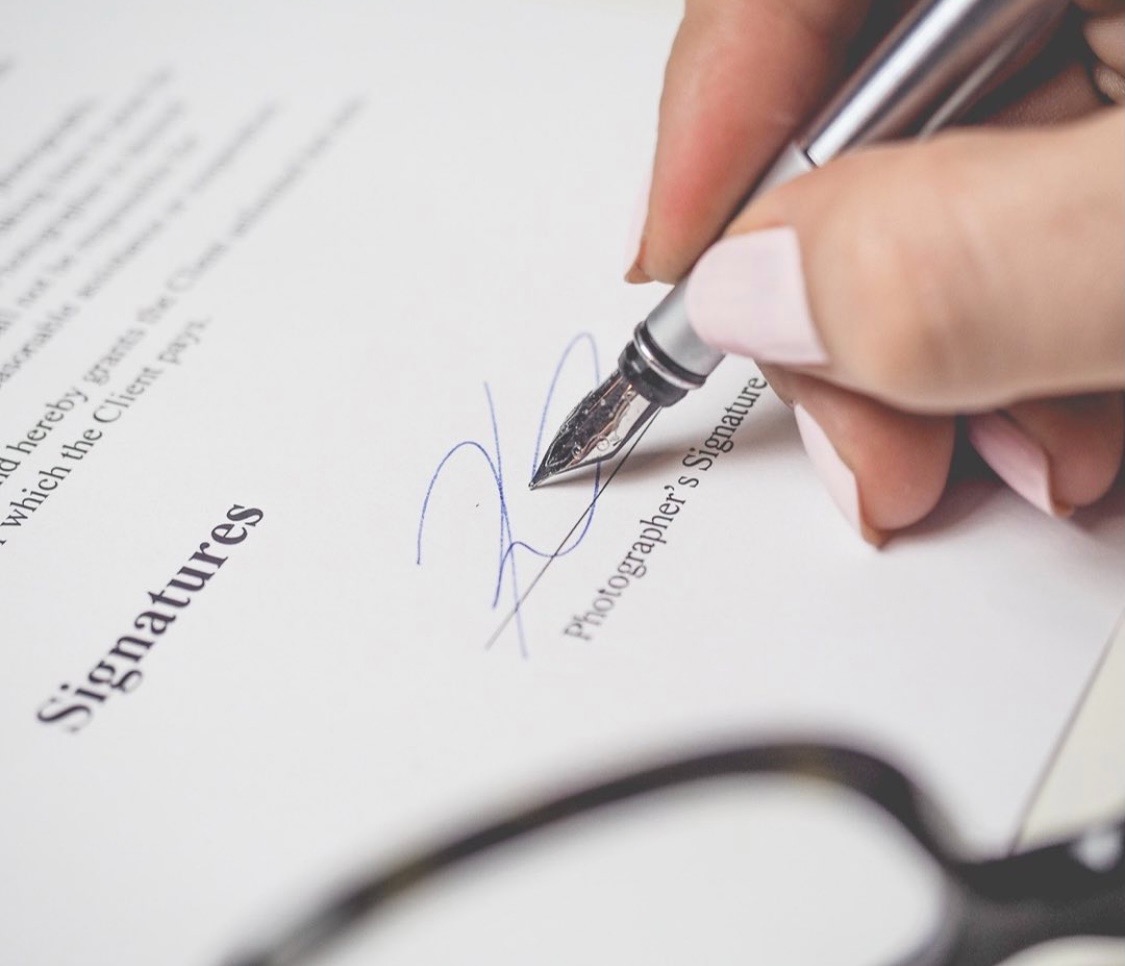 Podpis składany piórem wiecznym na dokumencie z napisem 'Signatures' oraz częściowym tekstem prawnym, z okularami w dolnej części kadru.