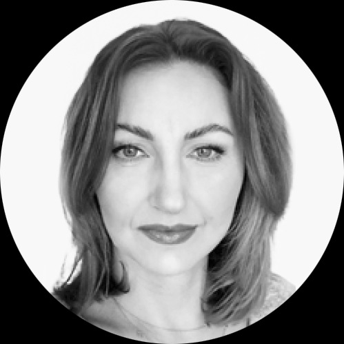 Czarno-biały portret kobiety z krótkimi włosami, skierowanej wprost, z delikatnym uśmiechem i widocznym naszyjnikiem.