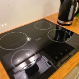 Błyszcząca, czarna płyta indukcyjna Hotpoint Ariston z czterema polami grzewczymi i czajnikiem elektrycznym Olive na drewnianym blacie kuchennym.