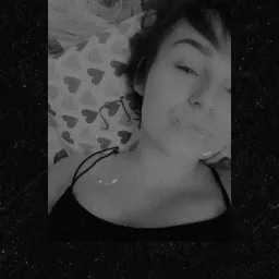 Czarno-białe selfie kobiety leżącej na poduszce w serduszka, widoczne ramiączko od koszulki.