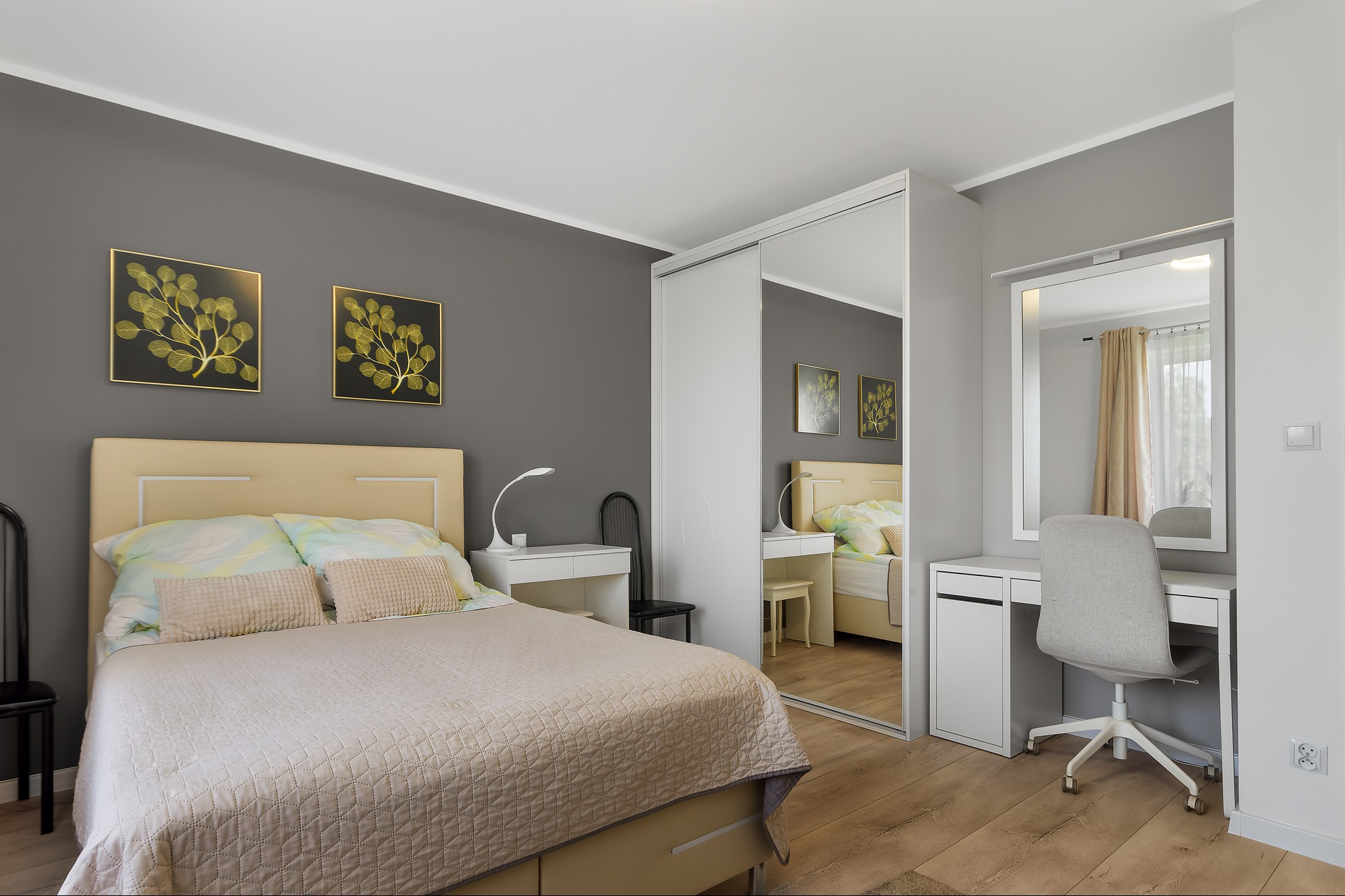 Nowoczesna sypialnia z łóżkiem w beżowej tonacji, biurkiem z lustrem, szafą przesuwną z lustrem i dekoracjami ściennymi z motywem roślinnym